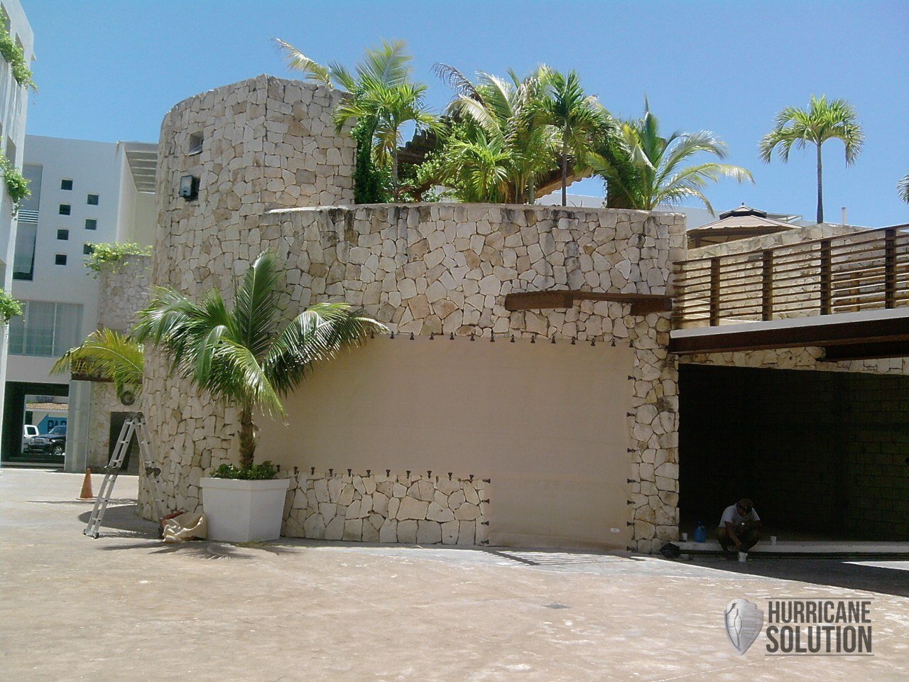 Hurricane Solution fabric screen covering an opening in a commercial stone wall beside palm trees.
