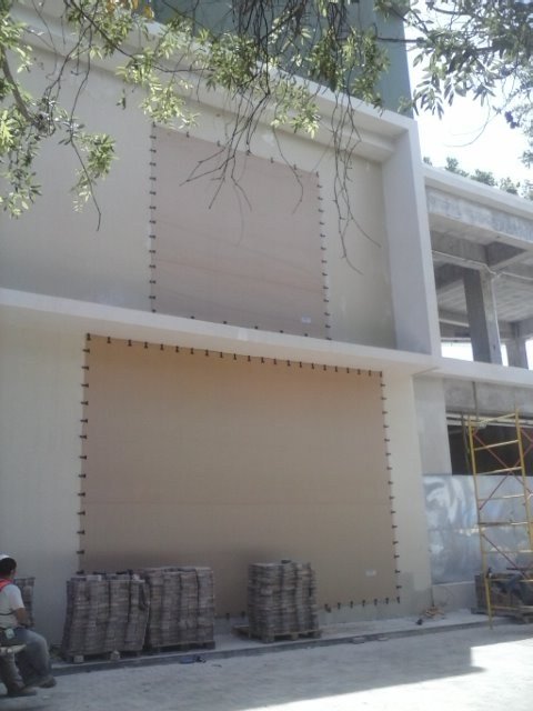 Fabric screens secured with clips over two levels of openings in a white facade, with work equipment in front.