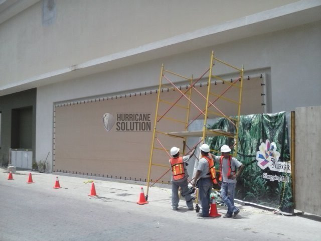 Workers wearing hard hats beside scaffolding in front of a Hurricane Solution screen fitted to a hotel facade.