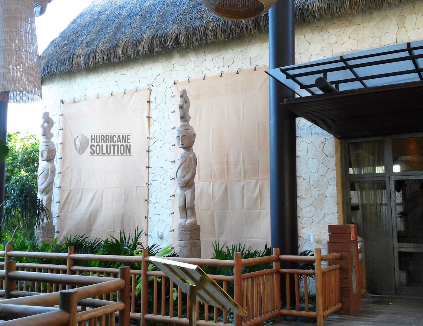 Hurricane Solution fabric screens covering openings beside a railed terrace with a thatched roof.