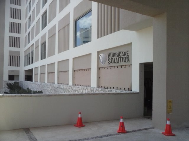 Hurricane Solution screens secured over ground-floor openings of a multistory hotel with a white facade.