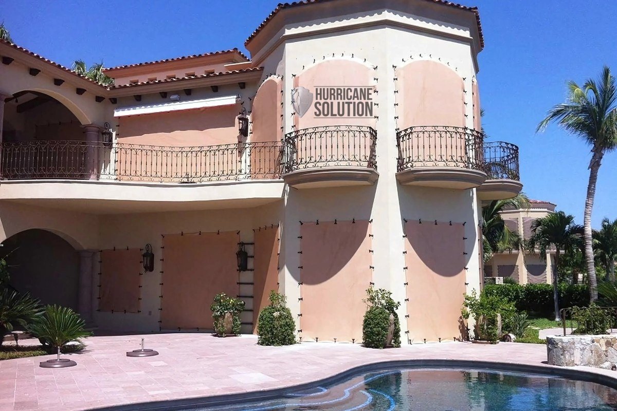 Hurricane Solution screens covering arched windows and doors of a two-story home beside a swimming pool.