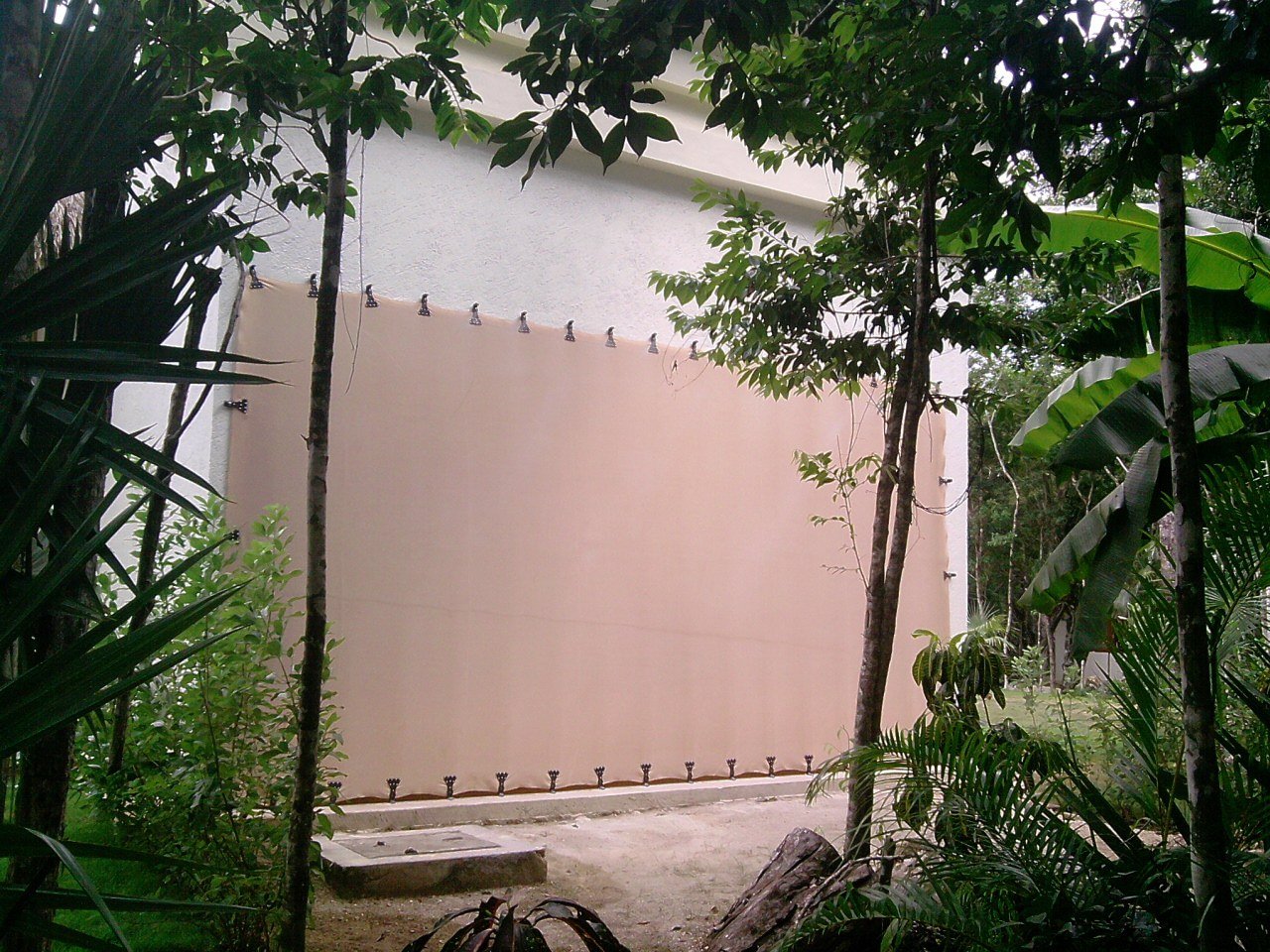 Fabric screen secured with perimeter clips across a tall residential opening among garden vegetation.
