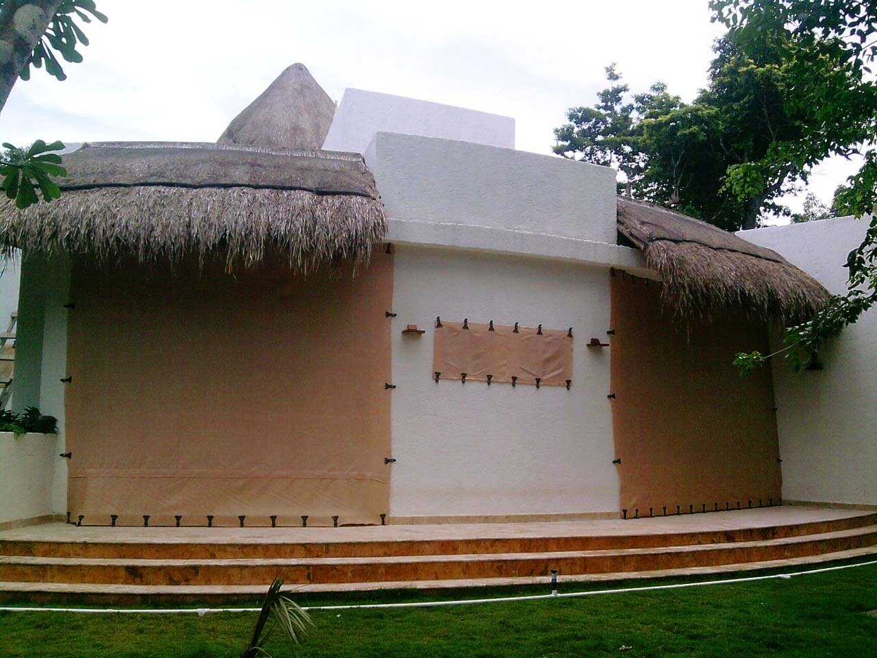 Fabric screens across a tall doorway and window of a white home with a curved porch and thatched roof.