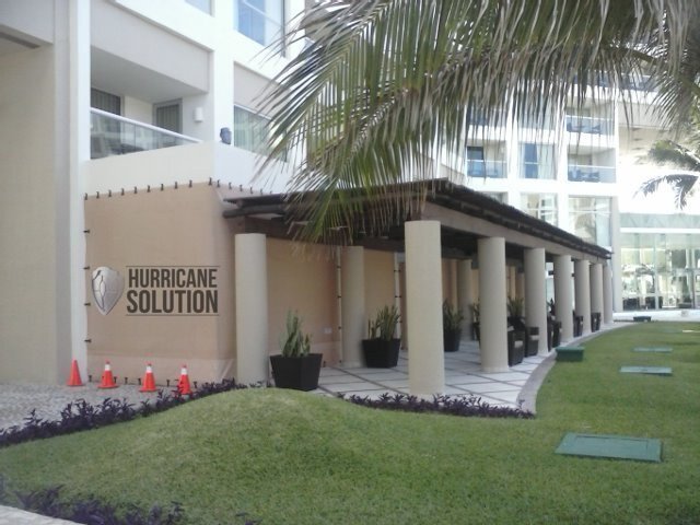 Hurricane Solution fabric covering openings of a white residential building beside a garden with palms.