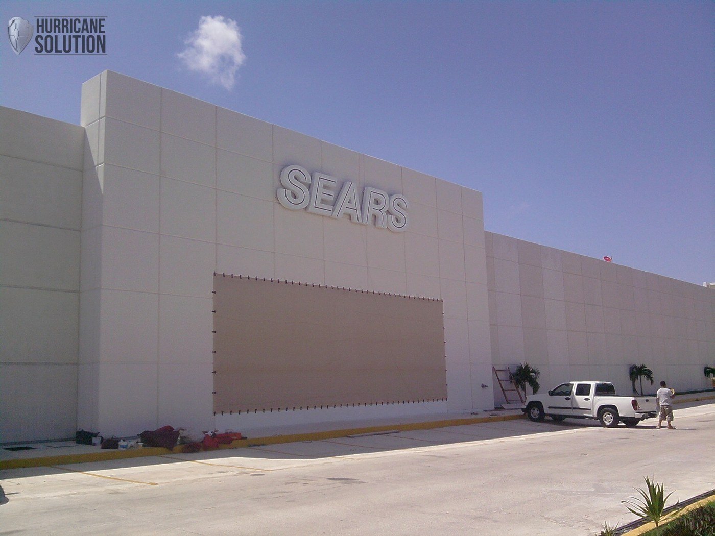 Sears facade with a fabric screen secured around a wide opening and vehicles in front.