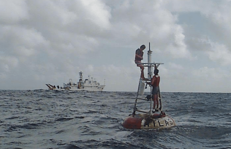 Dos hombres trabajan para reparar un sensor de viento en una boya oceánica de atmósfera tropical amarrada cerca de Hawaii en 1996. Al fondo, el barco Ka'imimoana de la NOAA.